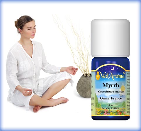 A bottle of VedAroma Myrrh essential oil shown with a young woman sitting cross-legged in meditation.