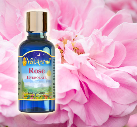 A bottle of VedAroma Rose Hydrosol is shown against a beautiful pink rose.